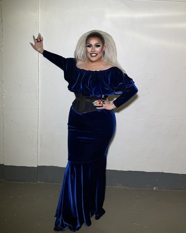 Abby Cummings in a navy velvet off-shoulder gown, one arm raised